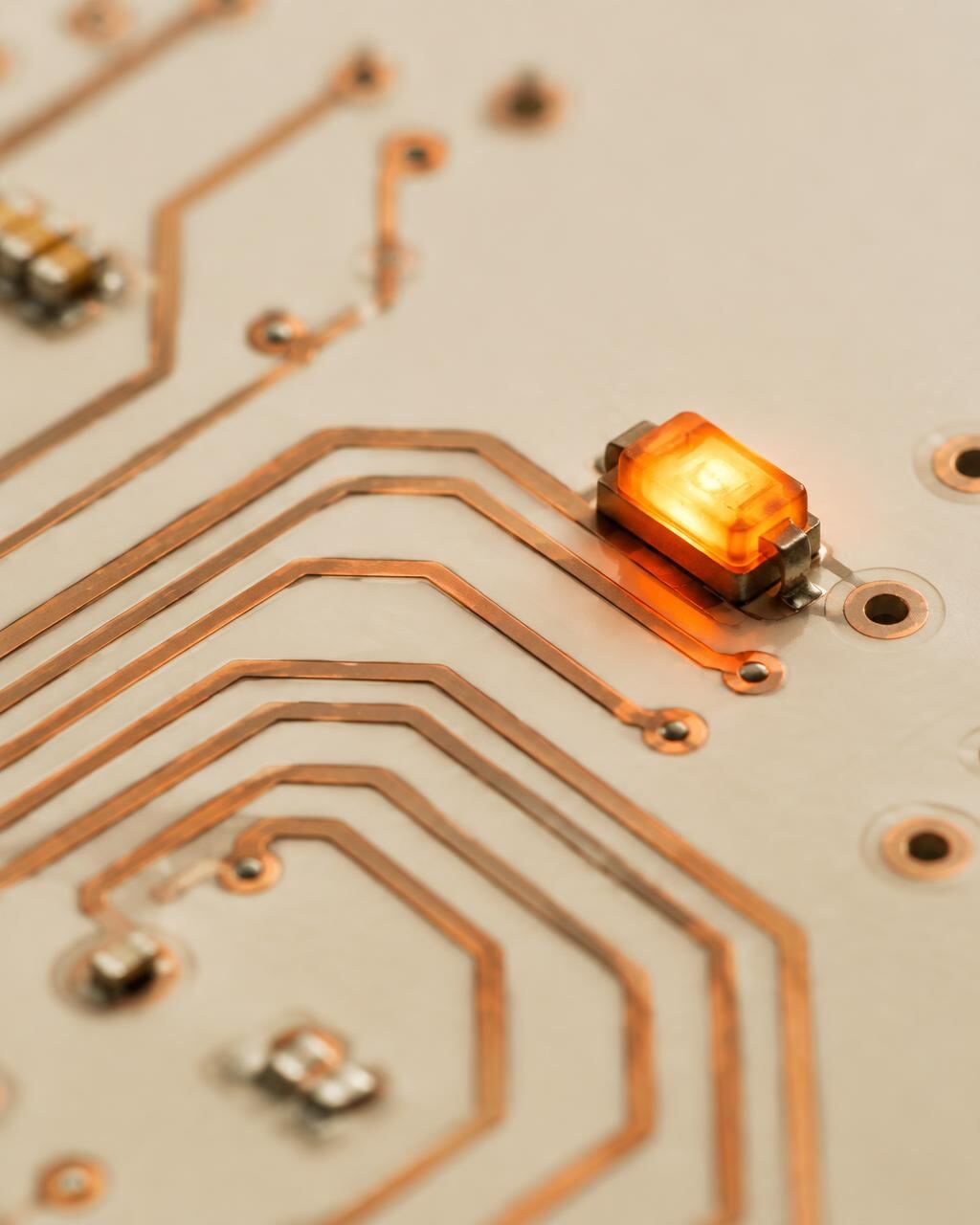 Macro view of copper circuit traces leading to a single glowing orange component